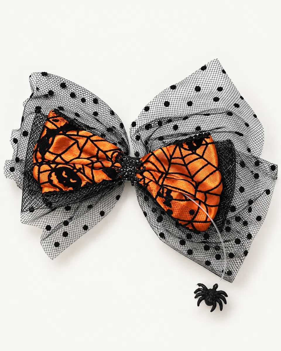 The spiderweb bow clip on a white background: orange satin printed with black spiderwebs and jack-o'-lantern faces, over black polka-dot tulle, with a little black spider on a thread